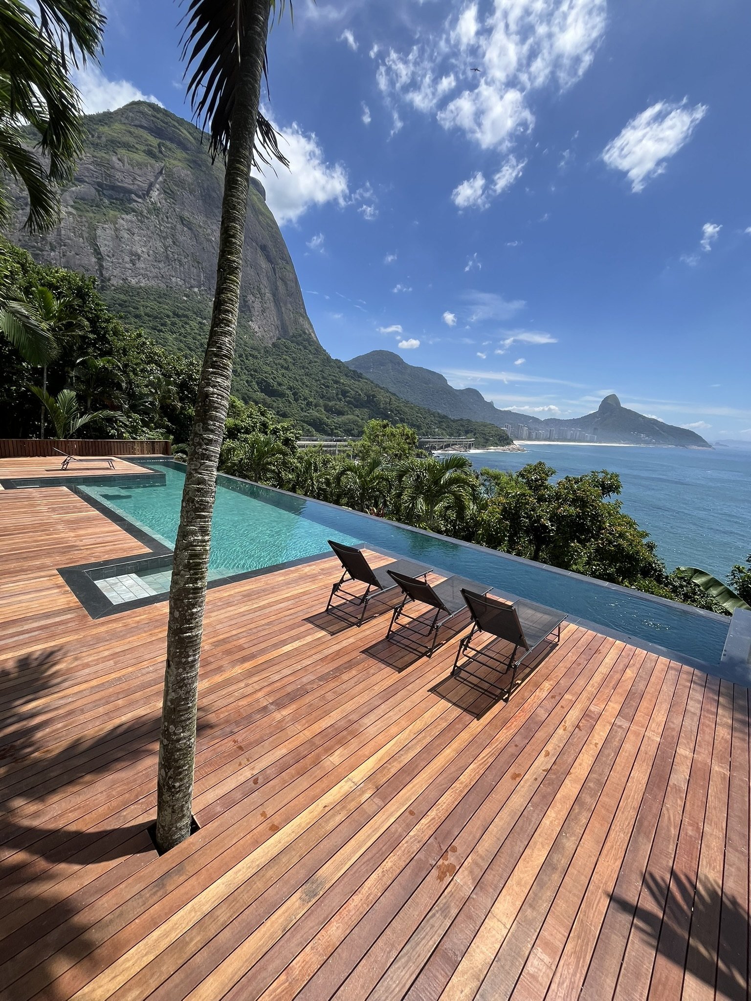 Deck de madeira e piscina com borda infinita diante da Pedra da Gávea e do mar