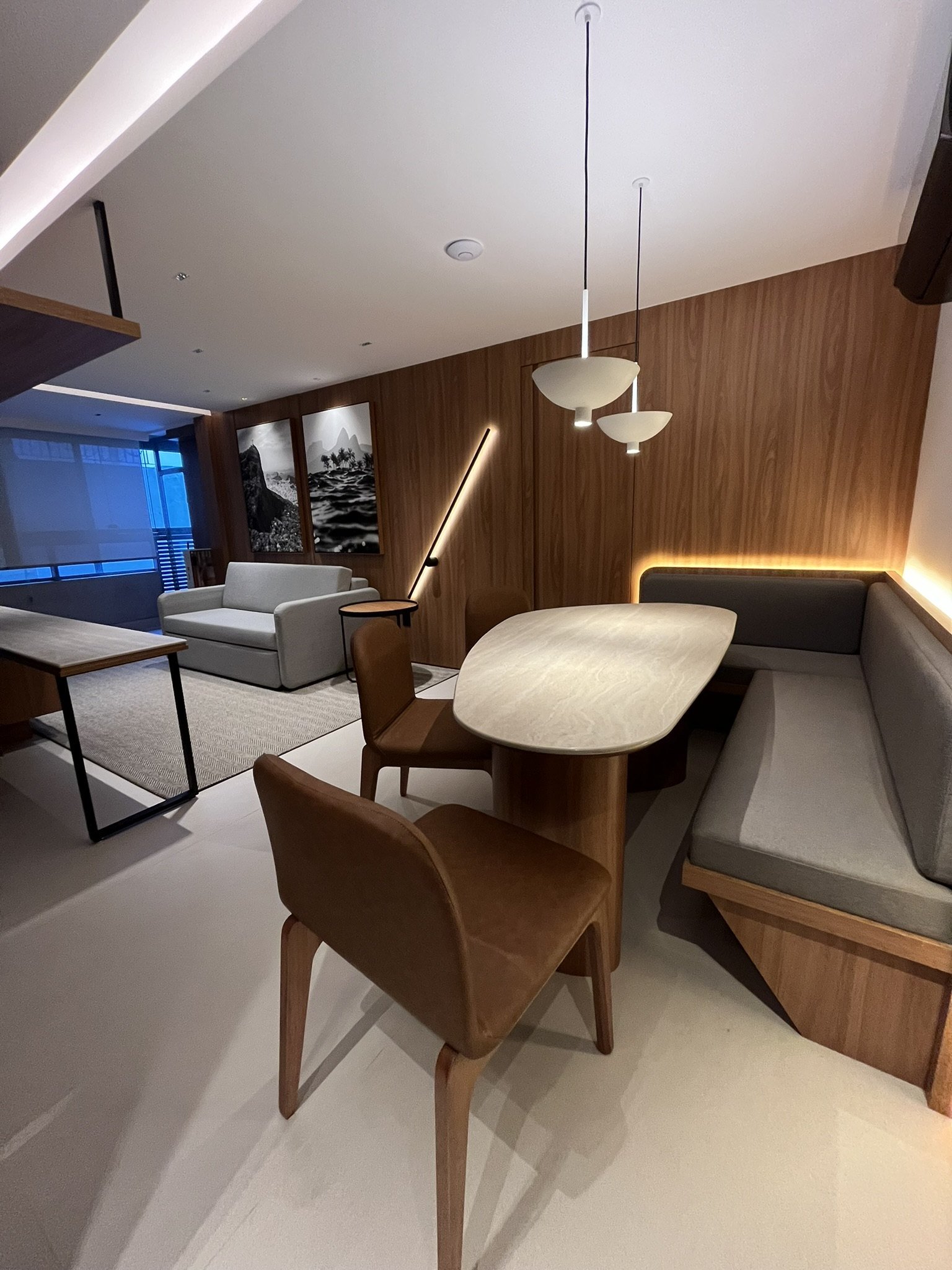 Sala de jantar com painel de madeira, mesa de pedra, banco estofado e pendentes